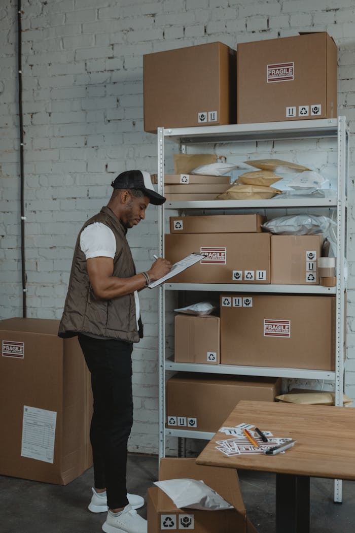 Business Man writing on a Paper while standing beside a Shelf of Boxes